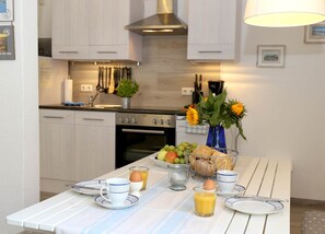 A modern kitchen with white cabinetry, a stainless steel range hood, and a dining area with a table set for breakfast.