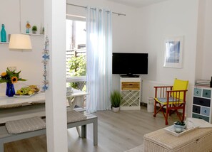 A living room with a TV, a dining table with a vase of flowers, and a chair.