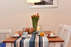 A breakfast table with a striped tablecloth, a candle, tulips, a bowl of muffins, and a glass of orange juice.
