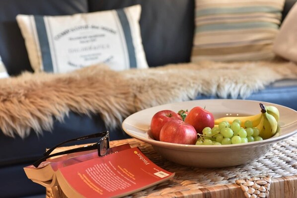 A bowl of fruit on a woven table, a book, and a pair of glasses.