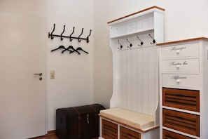 A room with a coat rack, a chest of drawers, and a small bench.