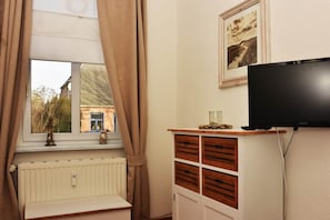 A room with a window, radiator, wooden cabinet, television, and a framed picture on the wall.