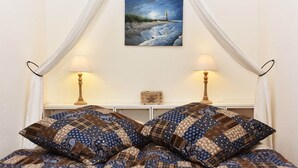 Un lit à baldaquin, deux lampes de chevet, un tableau représentant un phare et une petite boîte en bois posée sur la table de chevet.