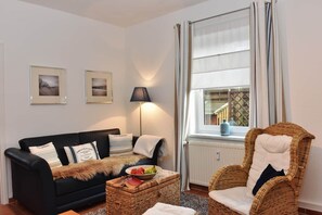 A living room with a black sofa, a wicker chair, a lamp, and a window with curtains.