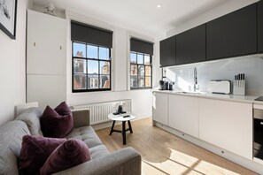 A modern kitchen with white cabinets, a dining table, and a sofa with purple cushions. - Marylebone’s Nest 1Bed (London)