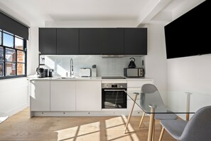 A modern kitchen with white cabinets, a Bosch oven, a microwave, and a kettle. - Marylebone’s Nest 1Bed (London)