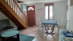A dining area with a table and chairs, a staircase, a sofa, and a small table. - L'Erable du Perche (Tourouvre au Perche)