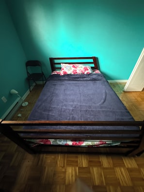A single bed with a wooden frame, a dark blue bedspread, and a floral pillow. - Bienvenu Chez toi! (Gatineau)