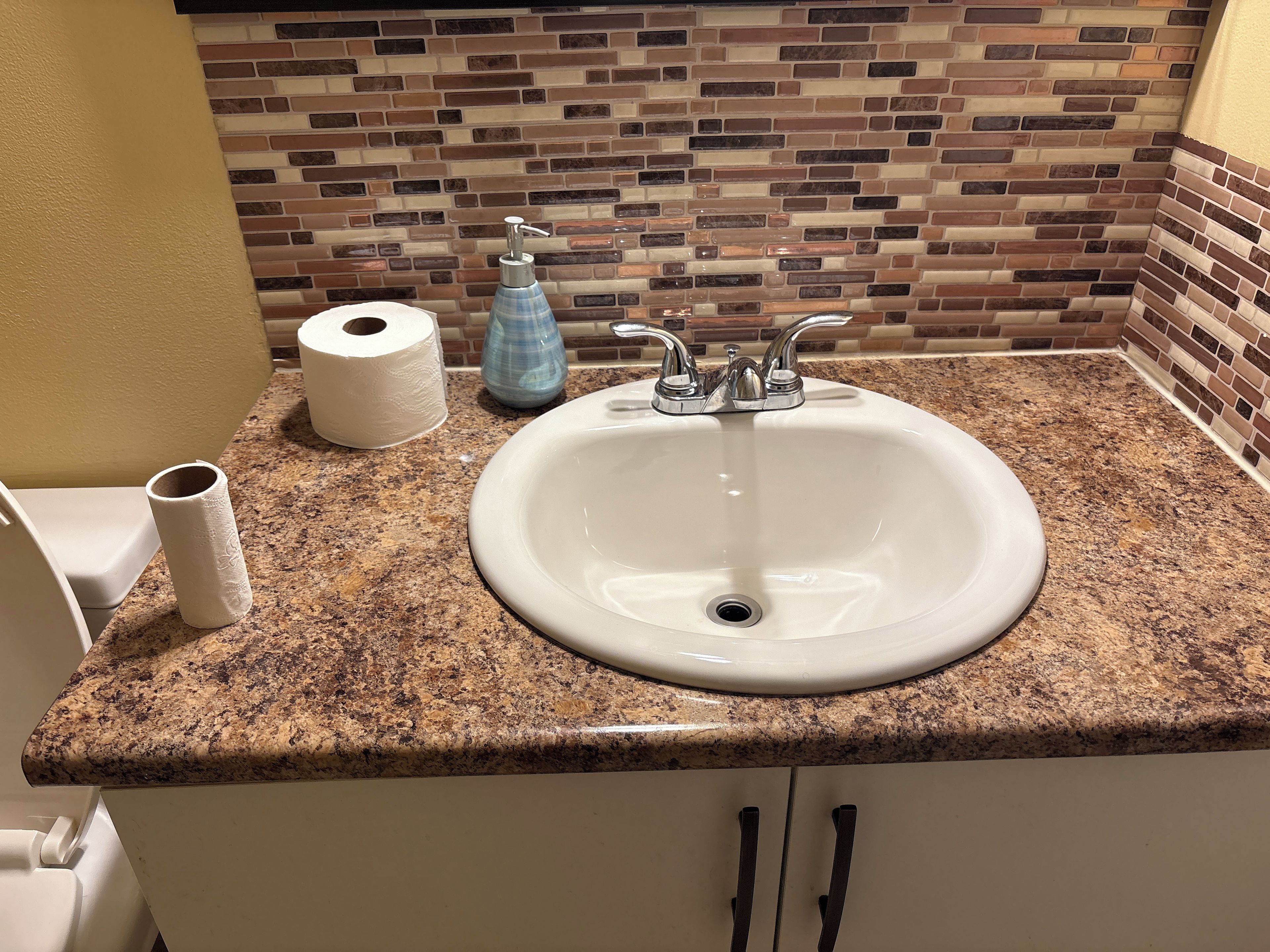A bathroom with a granite countertop, a white sink, a toilet, and a mosaic tile backsplash.
