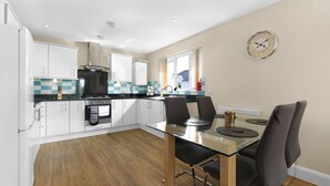 A modern kitchen with white cabinets, a glass dining table, and a wall clock. - Heathrow Living 2BDR 2BA Apt by 360 Stays - Apt 12 (Stanwell)