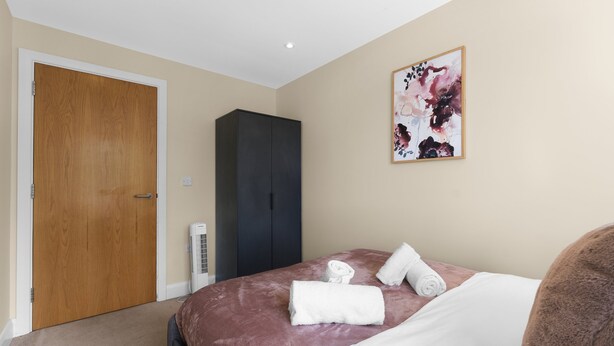 A bedroom with a bed, a wardrobe, a wall-mounted artwork, and a door. - Heathrow Living 2BDR 2BA Apt by 360 Stays - Apt 12 (Stanwell)