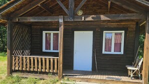 A wooden cabin with a porch, two windows, and a door. - The Chalets of Uza (Uza)