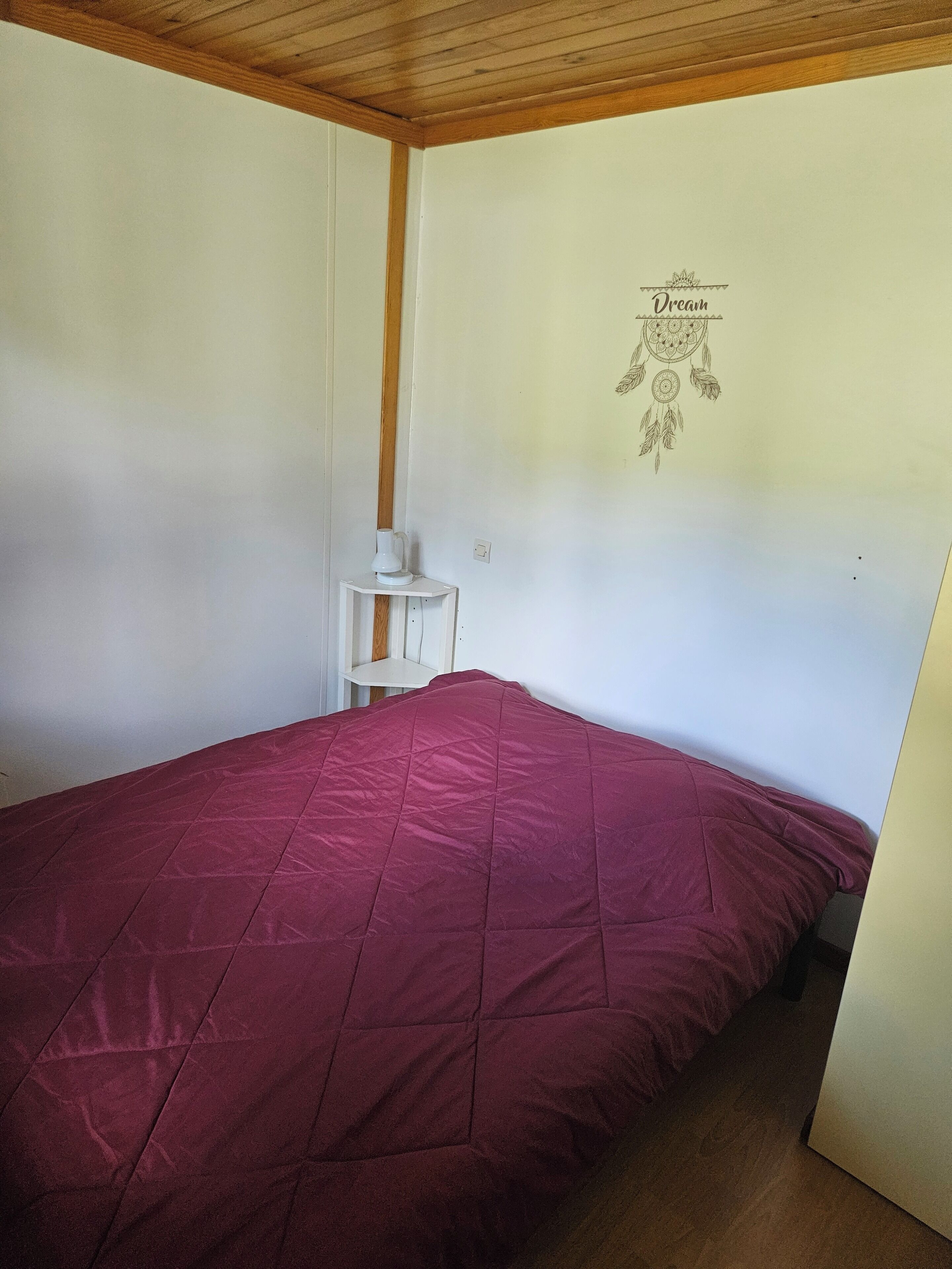 Una habitación con cama, una mesita de noche blanca, un muro con un símbolo de ensueño y vigas de madera en el techo.