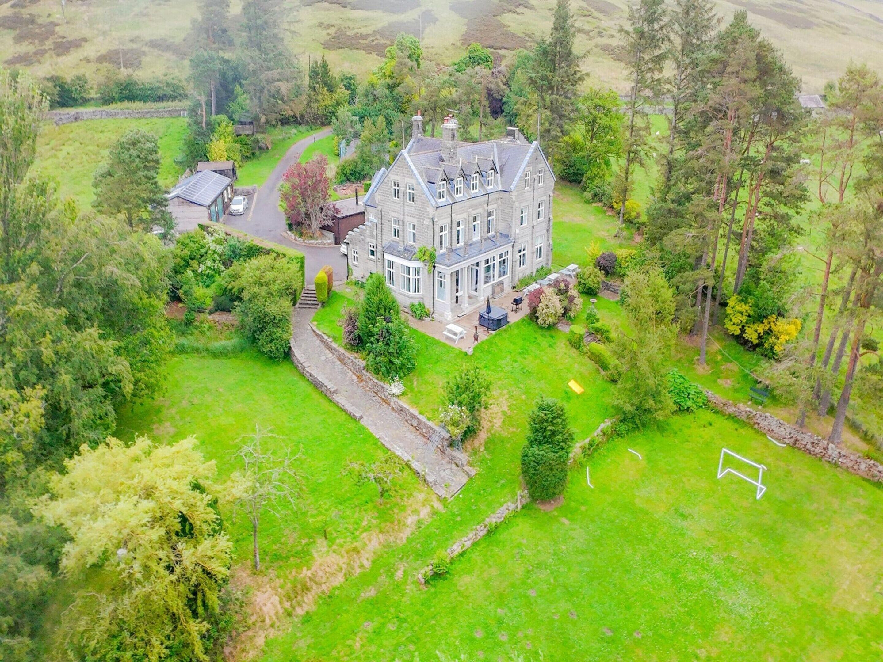 A large, historic stone house with a well-maintained lawn and a stone wall.