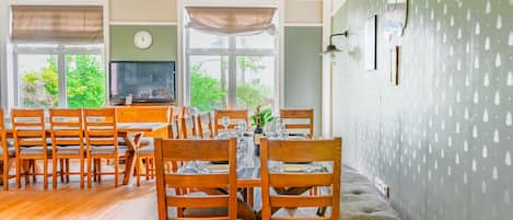 A dining area with wooden chairs and tables, a television, and a view of greenery outside.