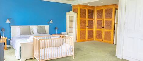 A bedroom with a blue wall, a crib, a bed, a wardrobe, and a door with a wooden panel design.