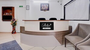A reception desk with a sign indicating it is a self-service area, a framed picture on the wall, and a chair to the right. - Collection O Rajkot Central Bus Terminal (Rajkot)