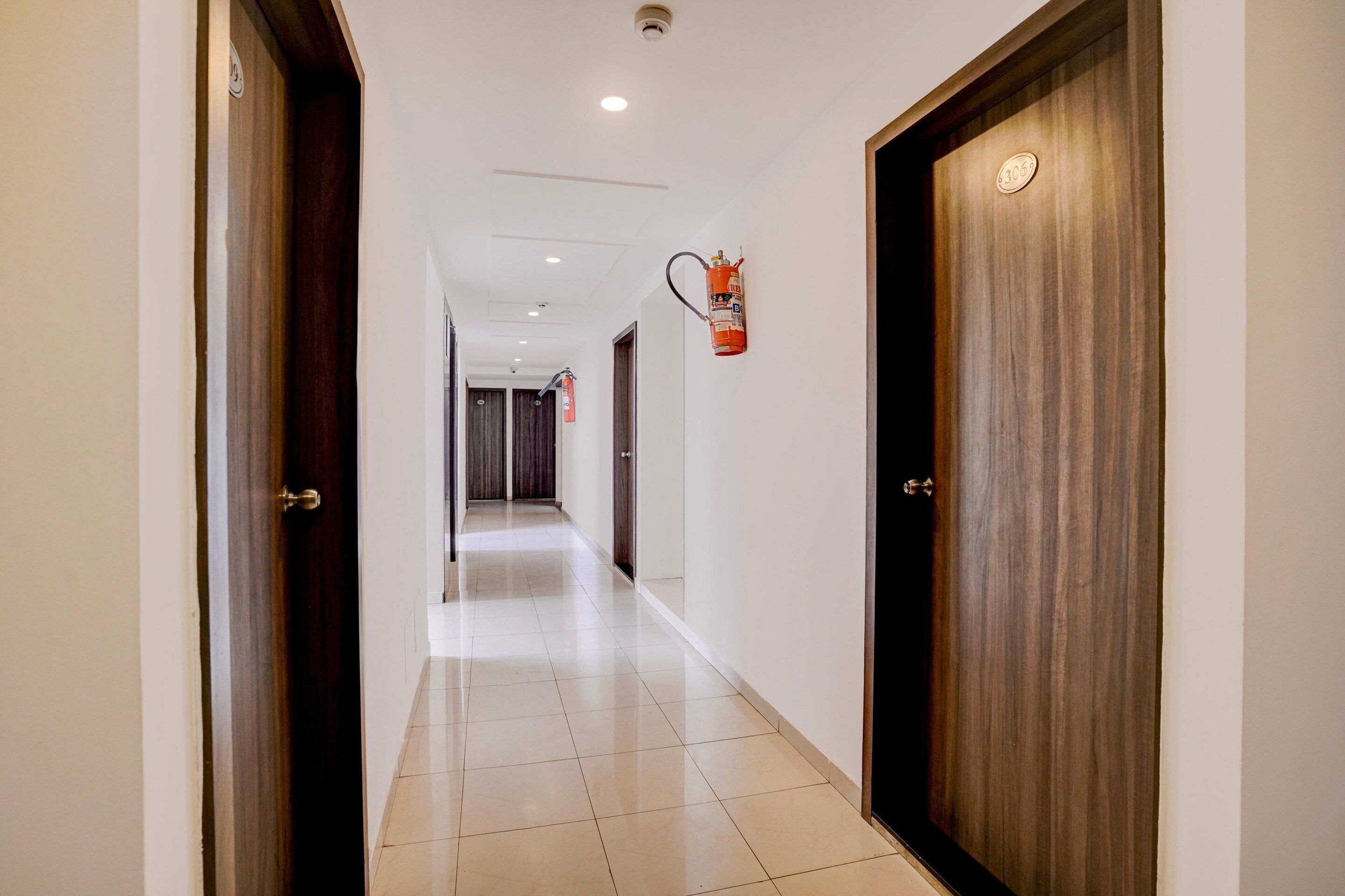 A corridor with doors on both sides, a fire extinguisher mounted on the wall, and a tiled floor.