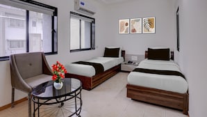 A hotel room with two beds, a chair, a table with a vase of flowers, and artwork on the wall. - Collection O Rajkot Central Bus Terminal (Rajkot)