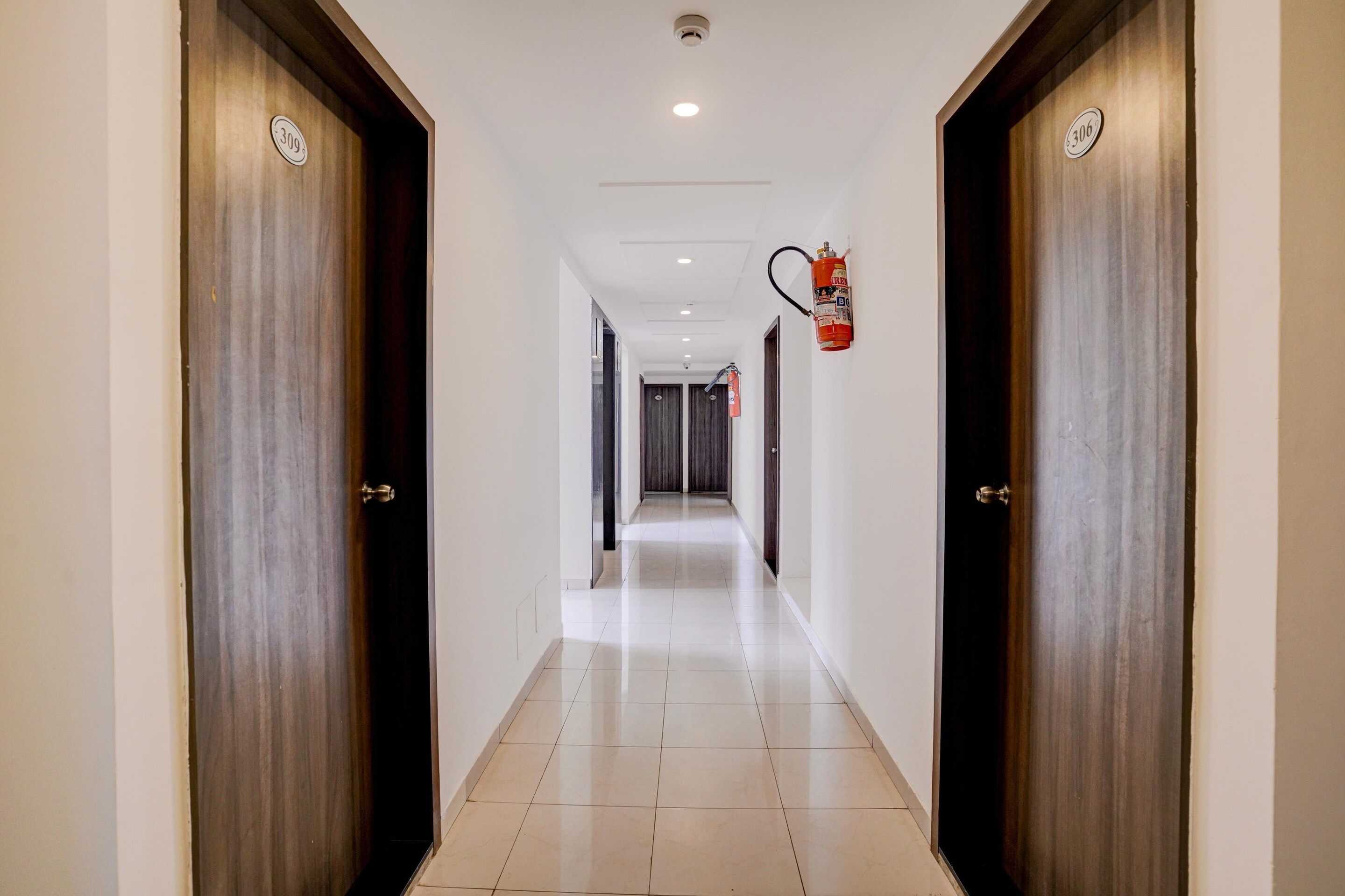 A hotel corridor with wooden doors, a fire extinguisher mounted on the wall, and a tiled floor.