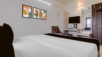 A hotel room with a bed, a chair, a desk with a flat-screen TV, a mirror, and framed artwork on the wall.