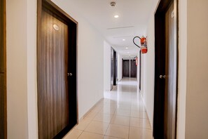 A hotel corridor with wooden doors, a tiled floor, and a fire extinguisher mounted on the wall.