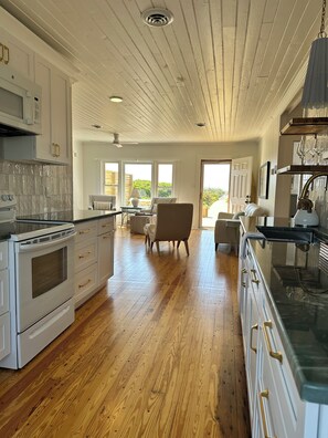 A kitchen with wooden flooring, white cabinetry, and a dining area with a chair and table. - NEW! Restored Oceanfront Cottage •  Vintage Charm • Walk to Dining (Topsail Beach)