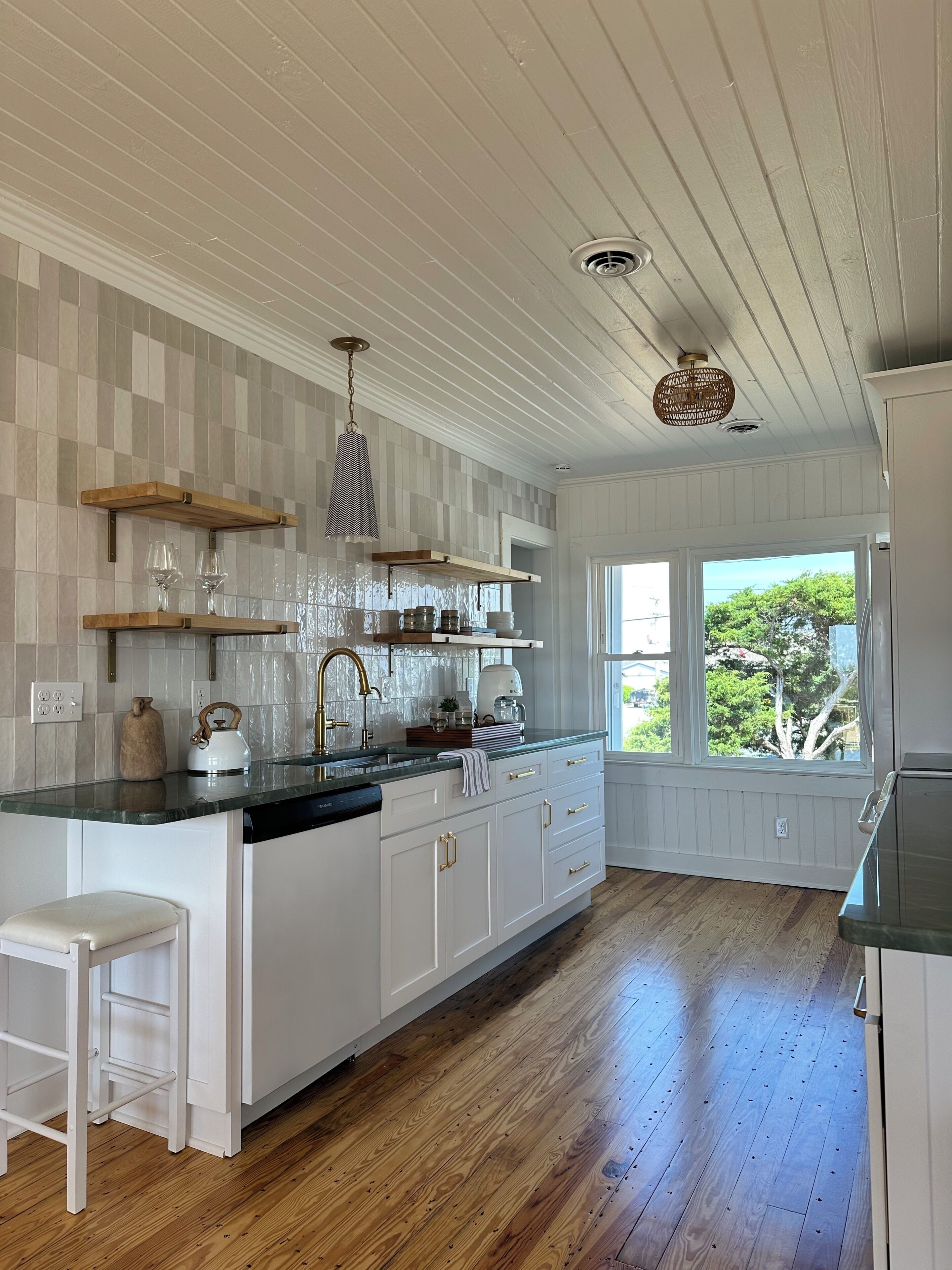 A kitchen with white cabinetry, wooden countertops, a built-in dishwasher, and a window with a view of trees.