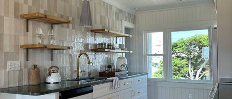 A kitchen with white cabinetry, wooden countertops, a built-in dishwasher, and a window with a view of trees.