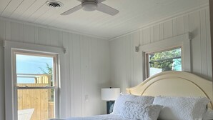 A bedroom with a bed, a ceiling fan, a window, and a view of the outside. - NEW! Restored Oceanfront Cottage •  Vintage Charm • Walk to Dining (Topsail Beach)