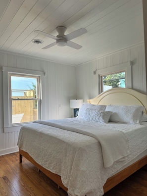 A bedroom with a bed, a ceiling fan, a window, and a view of the outside. - NEW! Restored Oceanfront Cottage •  Vintage Charm • Walk to Dining (Topsail Beach)