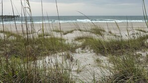 A beach with sand dunes, grass, and a pier in the distance. - NEW! Restored Oceanfront Cottage •  Vintage Charm • Walk to Dining (Topsail Beach)