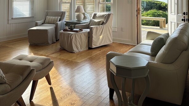 A spacious living room with a ceiling fan, large windows, and a view of the outdoors. - NEW! Restored Oceanfront Cottage •  Vintage Charm • Walk to Dining (Topsail Beach)
