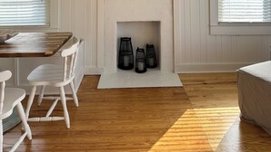 A room with a fireplace, a television mounted above it, and a view of the ocean through the window. - NEW! Restored Oceanfront Cottage •  Vintage Charm • Walk to Dining (Topsail Beach)