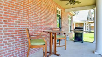 A covered patio with a brick wall, a ceiling fan, a table with chairs, and a grill.