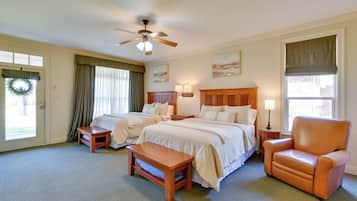 A hotel room with two beds, a wooden chair, a small table, a ceiling fan, and artwork on the walls.