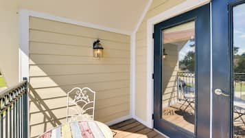 A porch with a wooden table and metal chair, a black door, and a small outdoor seating area with a metal railing.