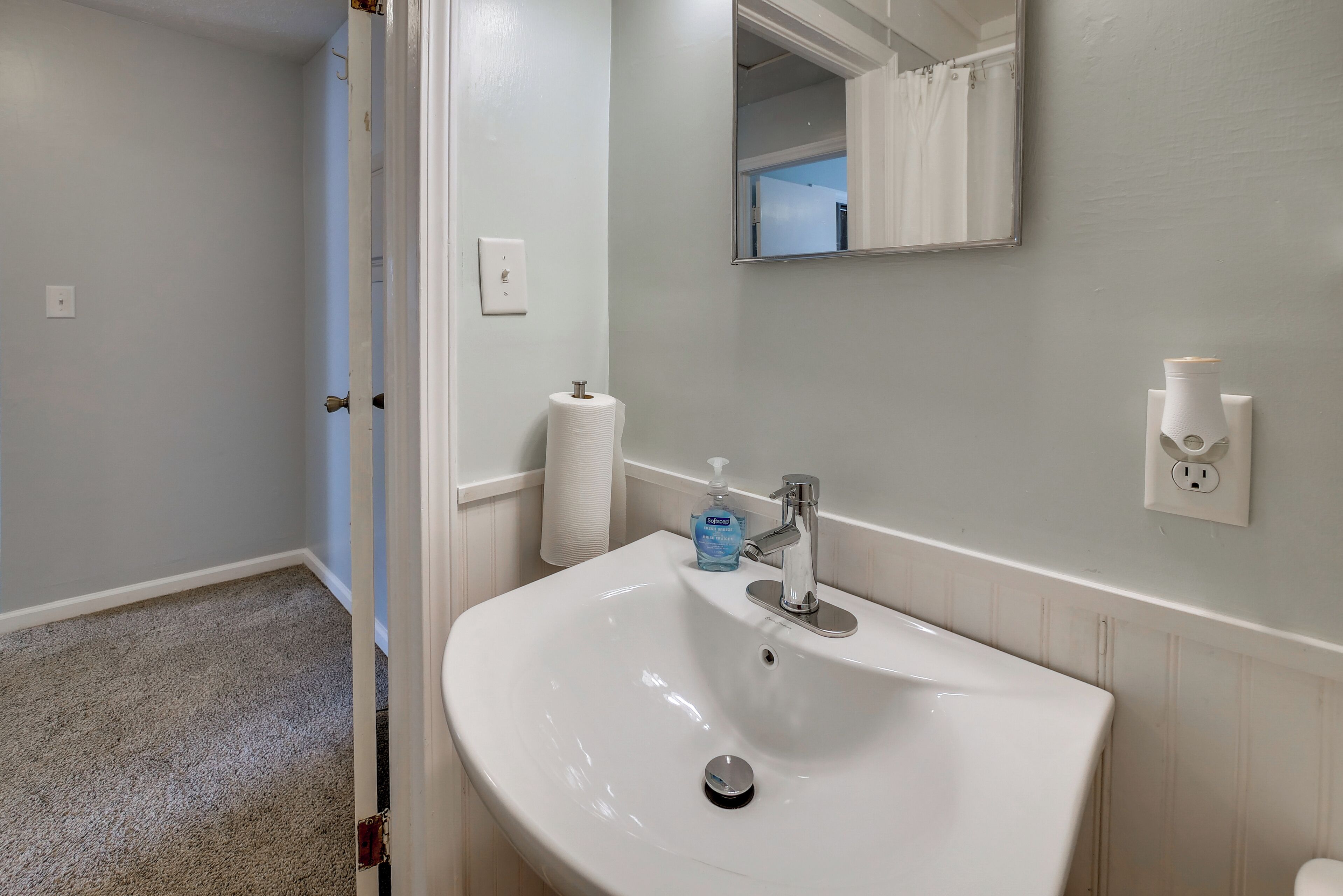 A bathroom with a white sink, a mirror, a towel dispenser, and a toilet paper holder.