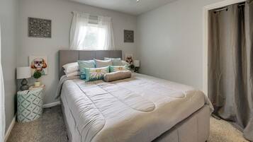 Un dormitorio con cama, mesitas de noche, una ventana con cortinas y una puerta.