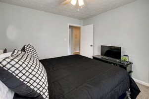 A bedroom with a bed, a television on a stand, and a door leading to another room.