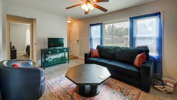 A living room with a sofa, coffee table, and ottoman, a television, and a ceiling fan.