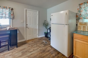 A kitchen with a white refrigerator, wooden flooring, a door, and a window with floral curtains. - 1 Mi to Fort Valley State College! Home w/ Grill (Fort Valley)