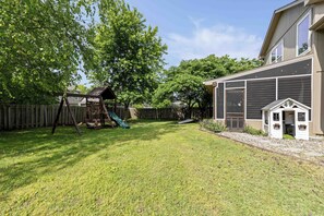 Ein Garten mit einer Holzspielanlage, einem kleinen Geräteschuppen und einem Haus mit Garage.