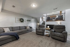 Ein Wohnzimmer mit einem grauen Sofa, zwei Sesseln, einem kleinen Tisch und einer Treppe, die in einen oberen Bereich führt.