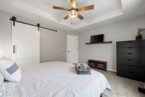 Ein Schlafzimmer mit Bett, Deckenventilator, Fernseher, Kommode und einer Pflanze.