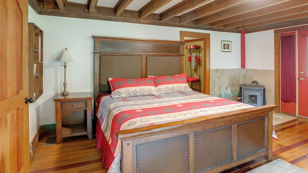 A bedroom with a wooden bed, a nightstand, a lamp, a red door, and a fireplace. - On Horse Farm! Home w/ Pond Access in Spring Creek (Spring Creek)