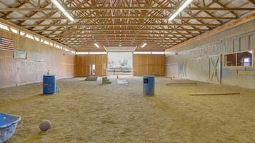 An indoor arena with a wooden ceiling, sandy floor, and a large open space.