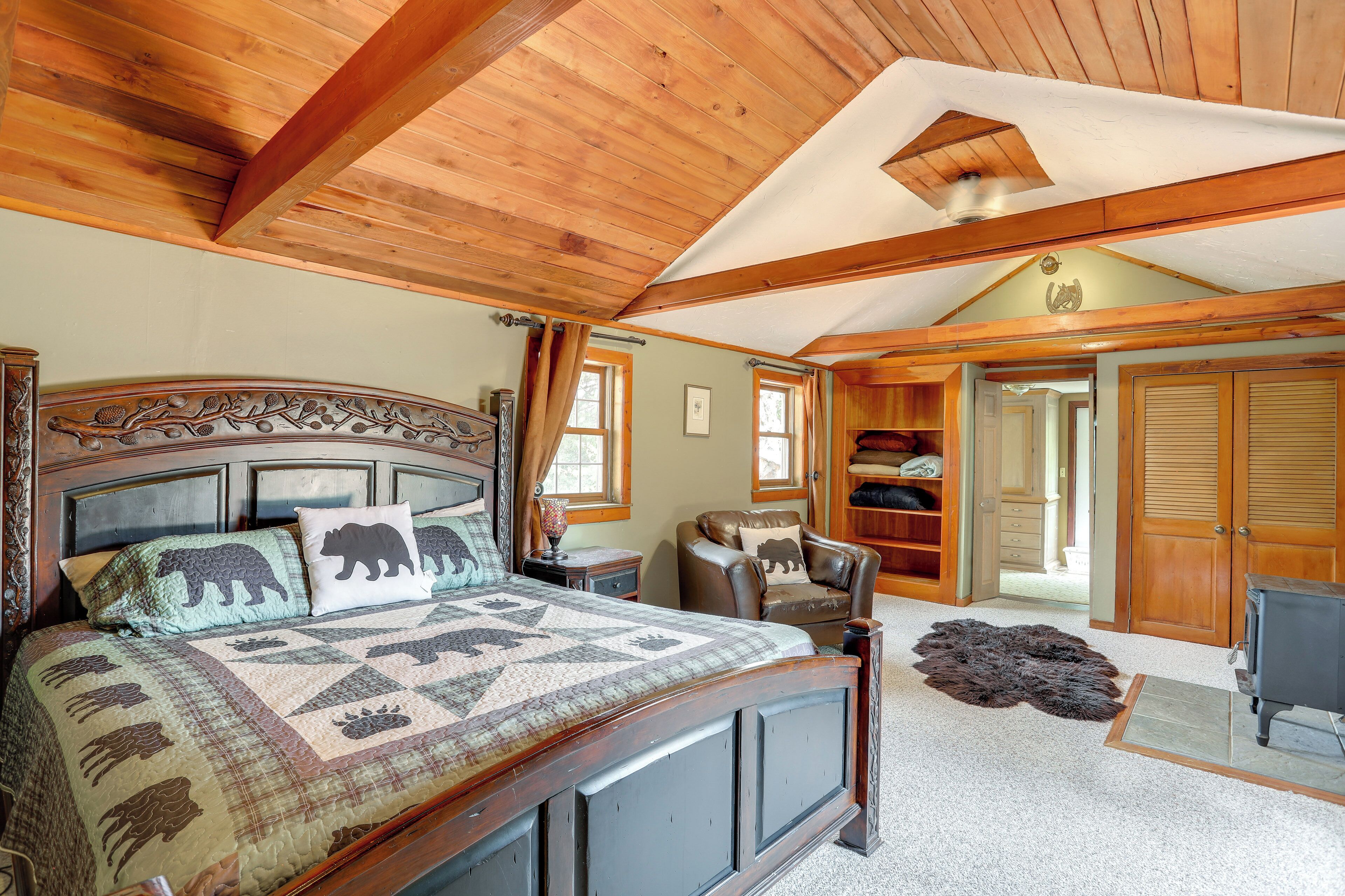 A bedroom with a wooden ceiling, a bed with a quilt, a chair, a lamp, and a closet.
