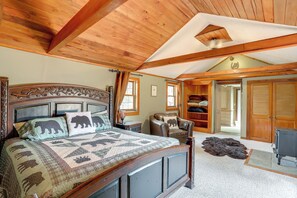 A bedroom with a wooden ceiling, a bed with a quilt, a chair, a lamp, and a closet.