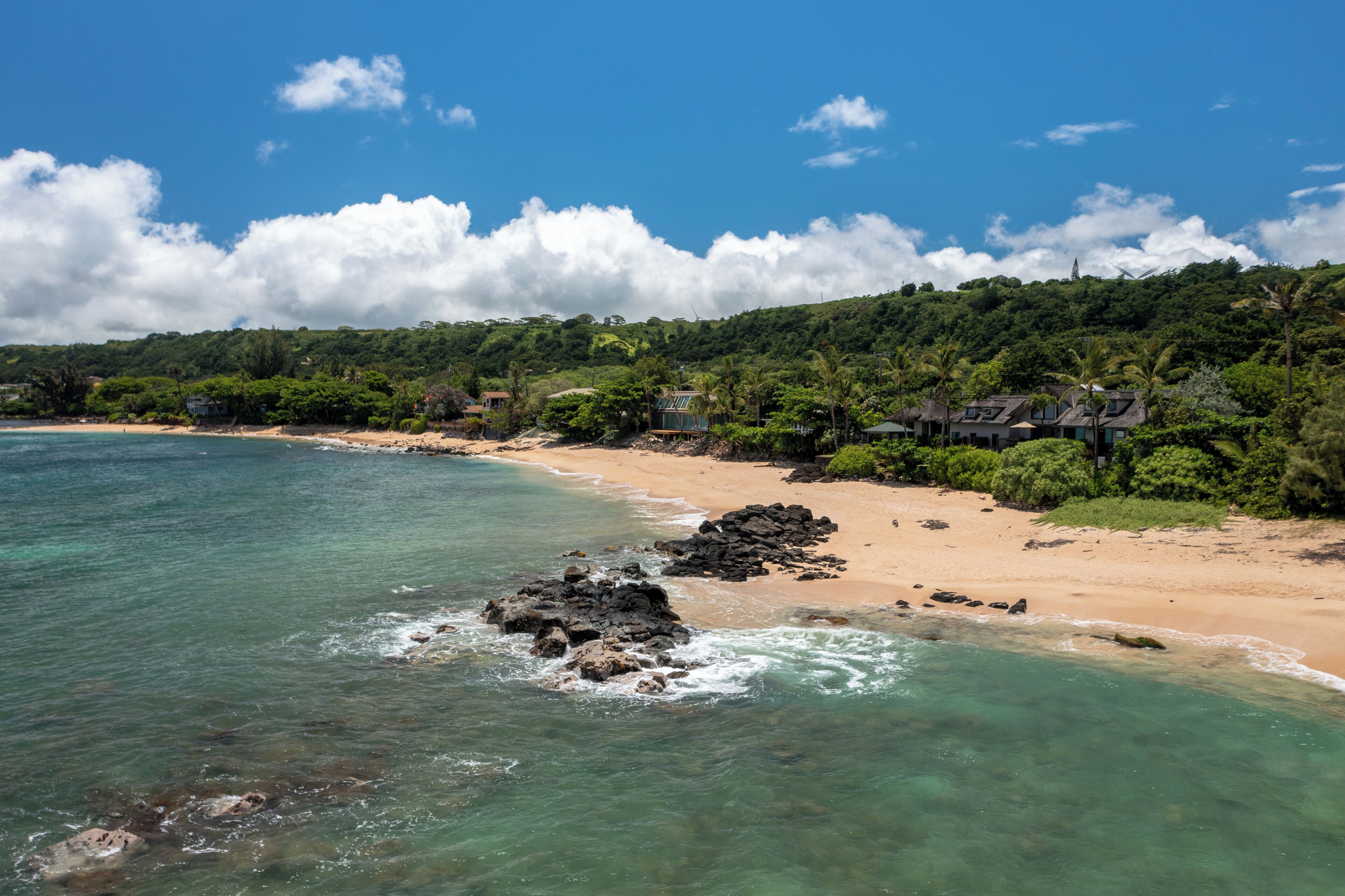 A coastal landscape with a beach, clear water, and lush greenery.